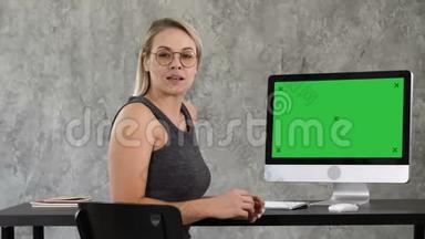 商务女士在办公室里和摄像机对着电脑屏幕说话。 绿屏模拟显示..